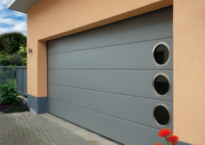 Une porte de garage sectionnelle à hublots à l’avantage de laisser la lumière naturel, installée par la société 3P HABITAT à Craponne 69290 Proximité de Lyon